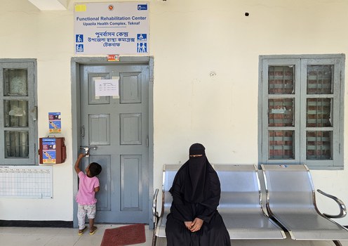 A Rohingya refugee who came to seek medical treatment sits in front of a locked room at a health care facility at the Teknaf Upazila Health Complex in Cox’s Bazar, Bangladesh, while her child plays in the background, Feb. 10, 2025.