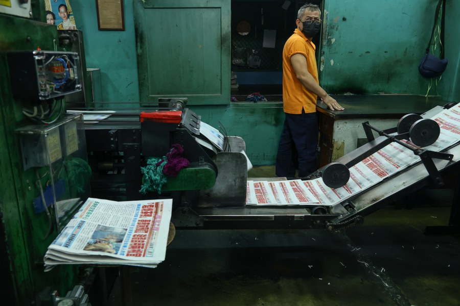 Copies of the final edition of Shi Jie Ri Bao (the Universal Daily News), a Chinese-language newspaper published in Thailand, flow off the press in Bangkok as a worker watches the progress, Dec. 30, 2024.