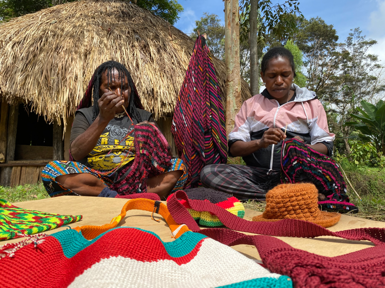 Magasalok Asso (kiri) merajut tas tradisional Papua noken bersama menantunya, Sisilia Asso, di depan rumah kayu yang disebut "honai" di Walesi, Papua Pegunungan, 14 Januari 2024. [Dandy Koswaraputra/BenarNews]